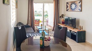 Un salón con una mesa de vidrio, dos sillas negras, un sofá, un televisor y un cuadro en la pared.