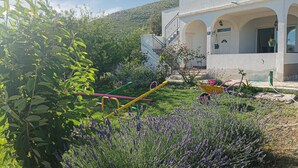 Un edificio blanco con arcos y un jardín con plantas de lavanda y un carretón amarillo.
