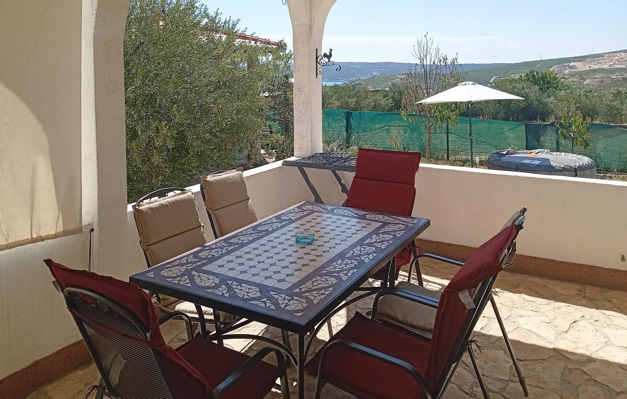 An outdoor patio with a table and chairs, a view of the countryside, and a green fence.