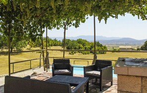 Une terrasse extérieure aménagée avec des meubles en osier, une piscine et une vue sur un vignoble et des montagnes lointaines.