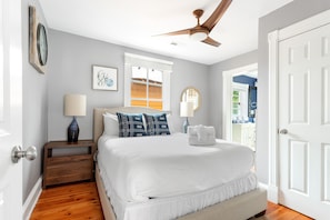 A bedroom with a large bed, a nightstand, a ceiling fan, and a window with blinds.