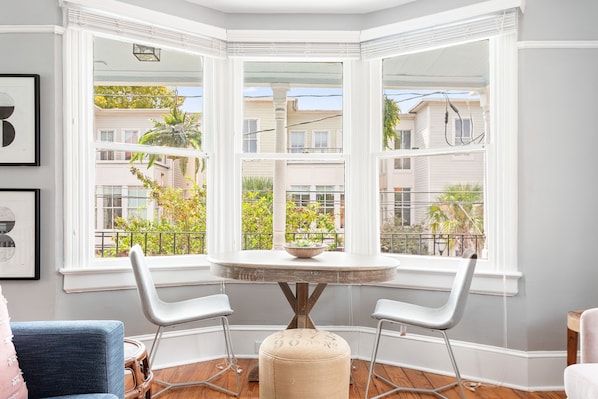 A corner room with a bay window, a round table, two chairs, and a small ottoman.