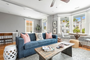A living room with a blue sofa, a wooden coffee table, and a view of the outside through large windows.