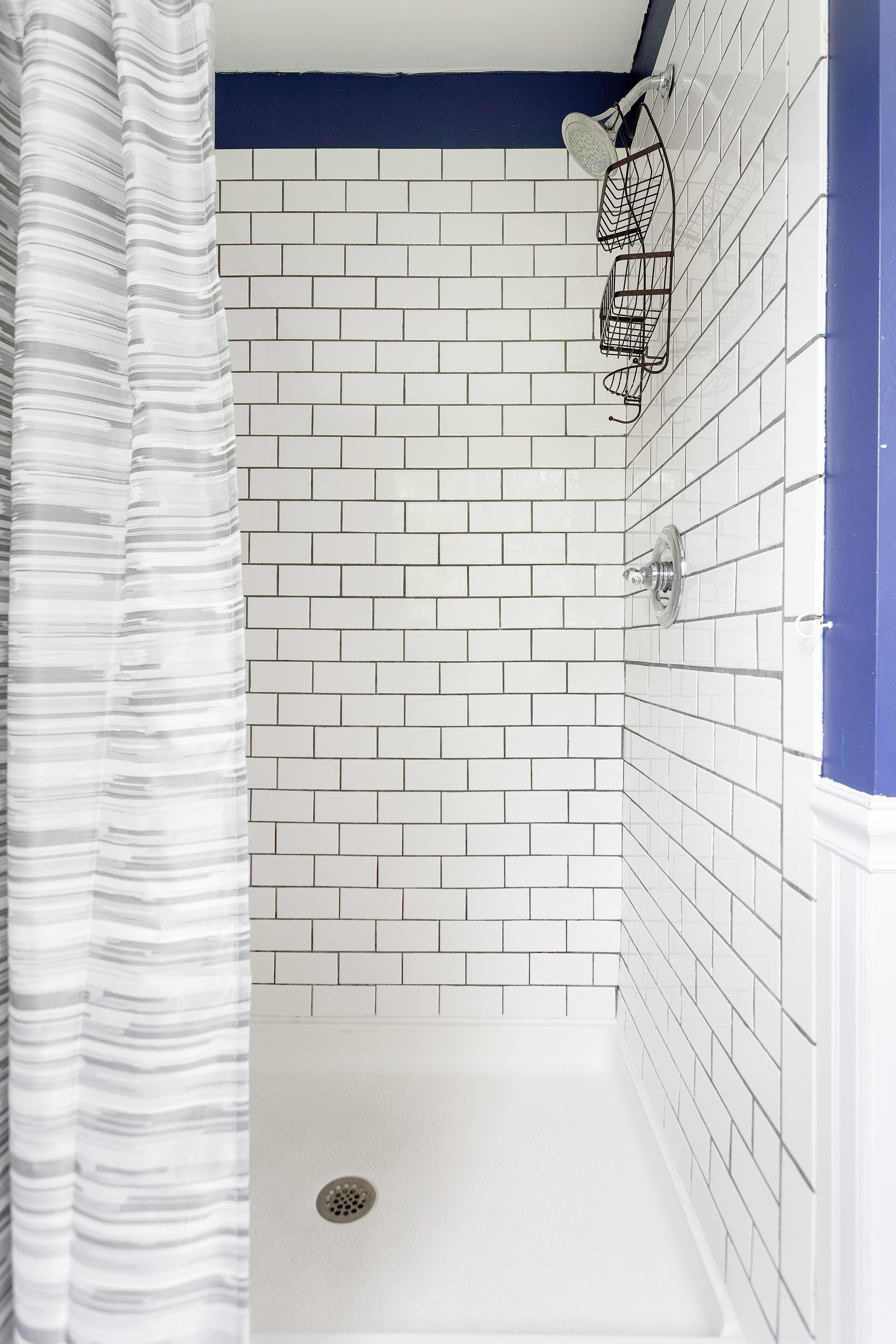Zona de ducha con paredes de azulejos blancos, desagüe y cabezal de ducha.