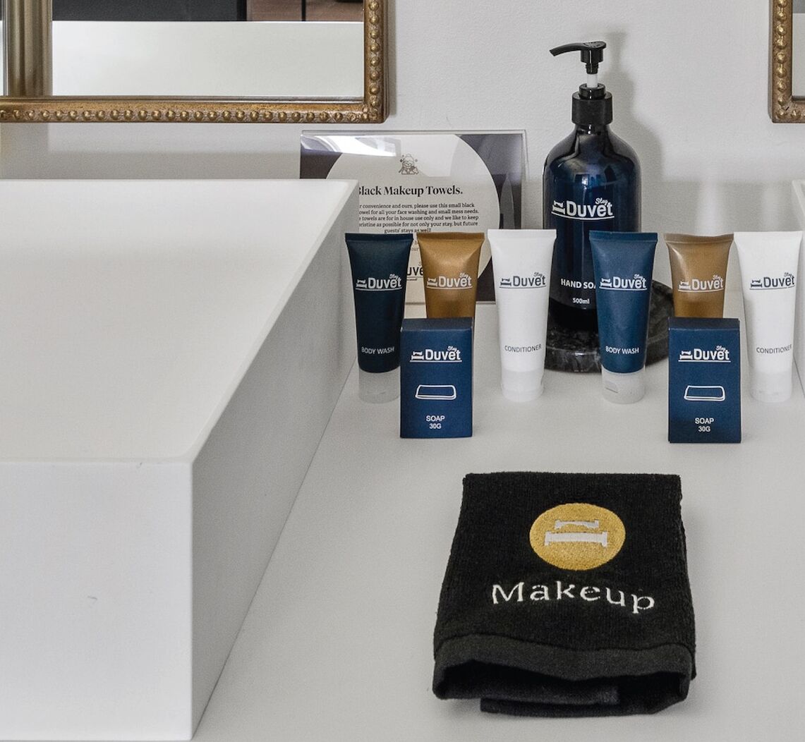 A bathroom vanity with a mirror, a black makeup towel, and various Duvet brand toiletries including body wash, soap, and conditioner.