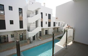 A modern building with a central swimming pool, multiple balconies, and a glass railing overlooking the pool. - Amazing apartment in Arenales del Sol (Arenales del Sol)