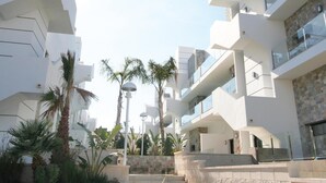 Un edificio moderno de varios pisos con balcones, una escalera central y palmeras alrededor.