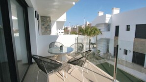 Un patio exterior moderno con una mesa de vidrio y sillas metálicas, una pequeña planta en maceta y vistas de edificios circundantes.