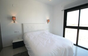 A bedroom with a large bed, two wall-mounted lamps, a nightstand, and a window with a view. - Amazing apartment in Arenales del Sol (Arenales del Sol)