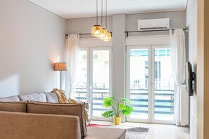 Una sala de estar con sofá, una lámpara, una planta y un ventanal corredera que da a un balcón.