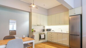 A modern kitchen with white cabinets, a stainless steel refrigerator, a wooden dining table with chairs, and a hanging pendant light. - 2 Bedroom & 2 Bathroom - 4mins Walk To Acropolis (Athina)