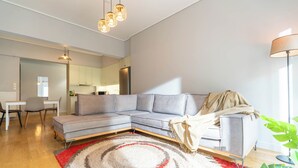 A modern living room with a sectional sofa, a dining area with a table and chairs, and a kitchen in the background. - 2 Bedroom & 2 Bathroom - 4mins Walk To Acropolis (Athina)