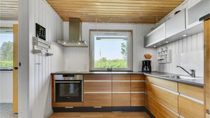 Et moderne køkken med træskabe, en integreret ovn og et vindue med udsigt til grøn vegetation.