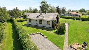 Et etplanshus med tegltag, omgivet af en velholdt græsplæne og en grusvej, der fører til indgangen.