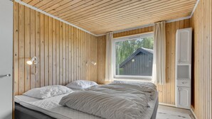 Et soveværelse med træloft, et stort vindue med gardiner, en seng med hvidt sengetøj og en træskab.