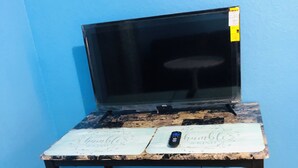 Ein kleiner, rustikaler Schreibtisch mit Fernseher, Fernbedienung und Stuhl darauf.