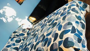 Ein Zimmer mit blauer Wand, einem gemusterten Bettbezug und einem gerahmten Bild an der Wand.
