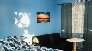 Ein Schlafzimmer mit einem Bett, einem kleinen runden Tisch, einem Bild an der Wand und einem Fenster mit Vorhängen.