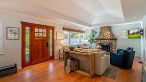 A spacious living area with a stone fireplace, wooden flooring, and a cozy seating arrangement. - Montecito Craftsman | Walk to Beach, Hot Tub, Bikes, Game Room & EV Charging (Montecito)
