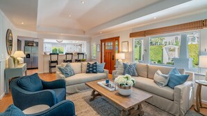 A spacious living room with a sofa set, a coffee table, and a view of the kitchen and garden. - Montecito Craftsman | Walk to Beach, Hot Tub, Bikes, Game Room & EV Charging (Montecito)