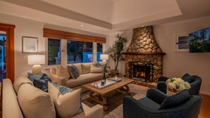 A cozy living room with a stone fireplace, a large window, and a comfortable seating area. - Montecito Craftsman | Walk to Beach, Hot Tub, Bikes, Game Room & EV Charging (Montecito)