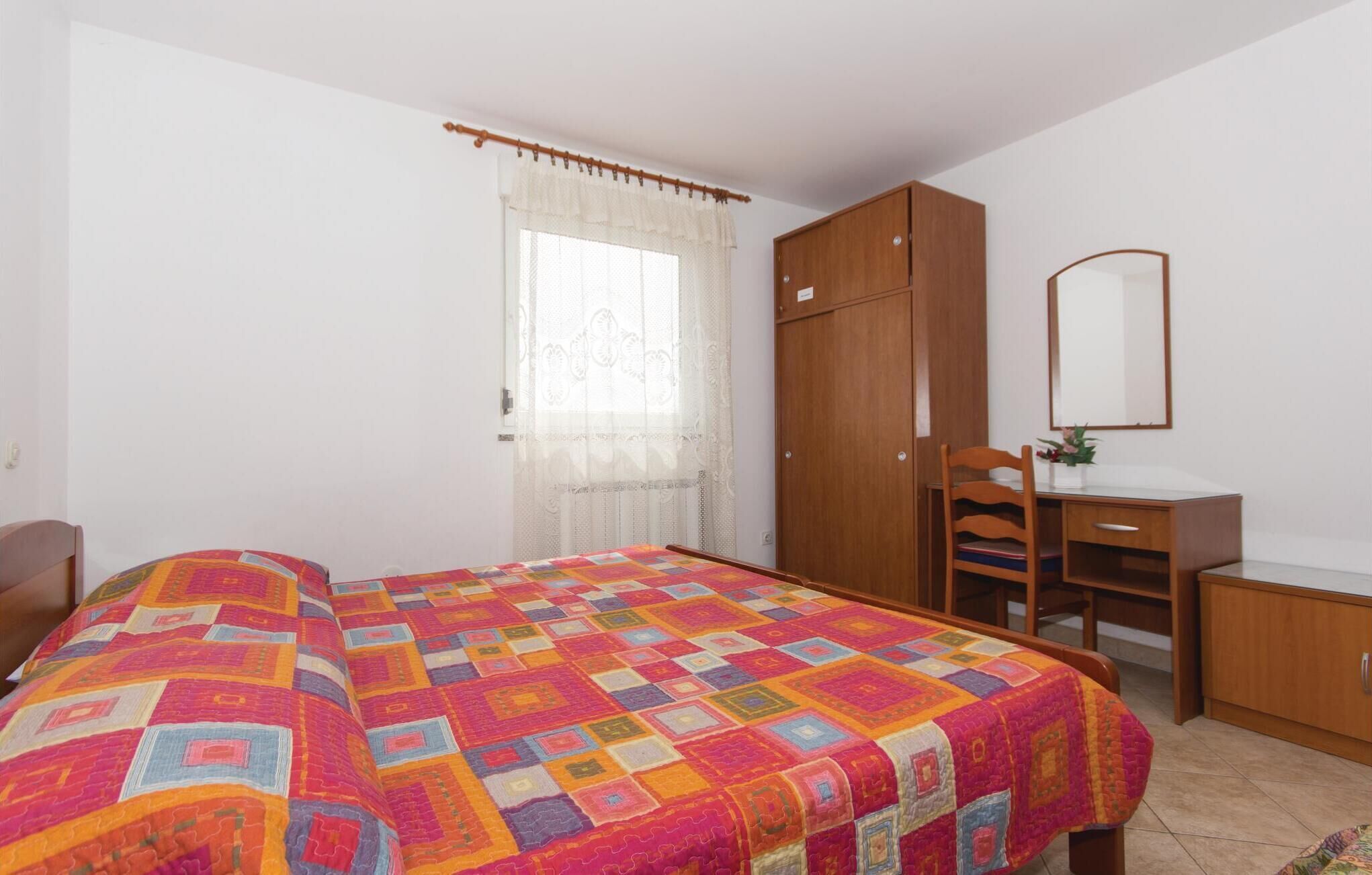 Een slaapkamer met een bed, een bureau, een stoel, een kledingkast en een raam met gordijnen.