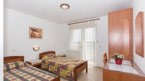 A bedroom with two beds, a wooden wardrobe, a bedside table, a wall-mounted lamp, and a window with curtains. - Awesome apartment in Pula with house sea view (Pula)