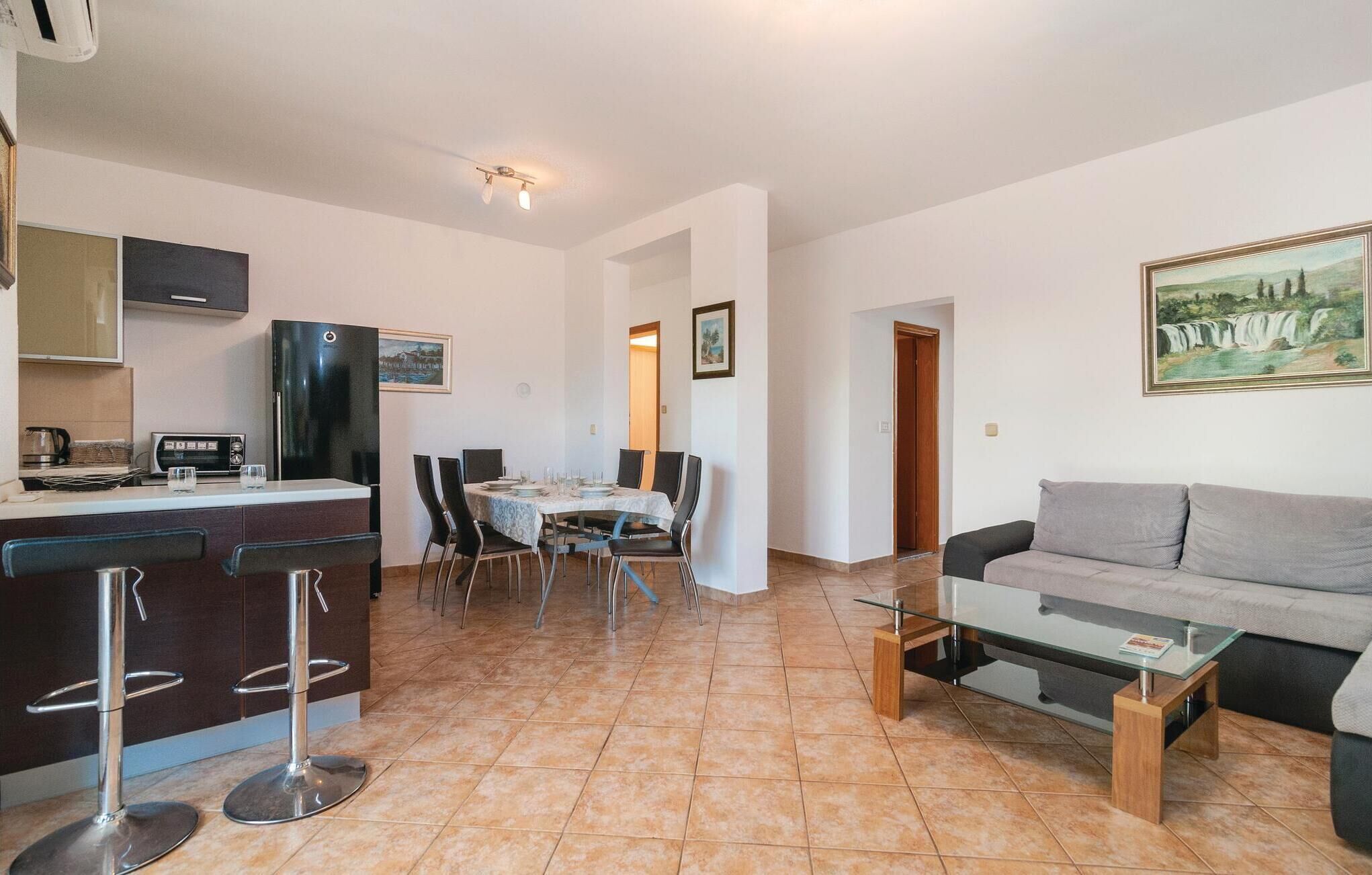 Una sala de estar moderna con un sofá gris, una mesa de centro de vidrio y un comedor con mesa lista para cuatro.