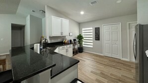 A modern kitchen with a black granite countertop, white cabinets, and a stainless steel refrigerator.