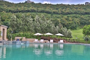 A swimming pool with lounge chairs and umbrellas, surrounded by lush greenery and a golf course in the background. - Oxford Golf Resort (Pune)