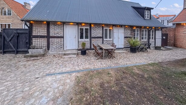 A two-story stone building with a metal roof, outdoor seating, and a paved courtyard.