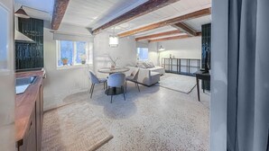 A modern living room with a dining area, wooden beams, a sofa, and a TV.