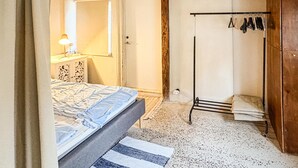 A bedroom with a bed, a bedside table, a mirror, a wardrobe, and a hanging clothes rack.