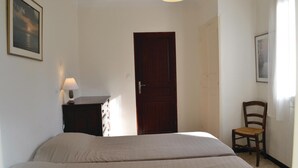 Un dormitorio con cama, una silla, un escritorio con lámpara, una puerta y un cuadro en la pared.