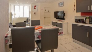 Ein modernes, helles Zimmer mit Esstisch, Stühlen, Fernseher und einer Küchenzeile.