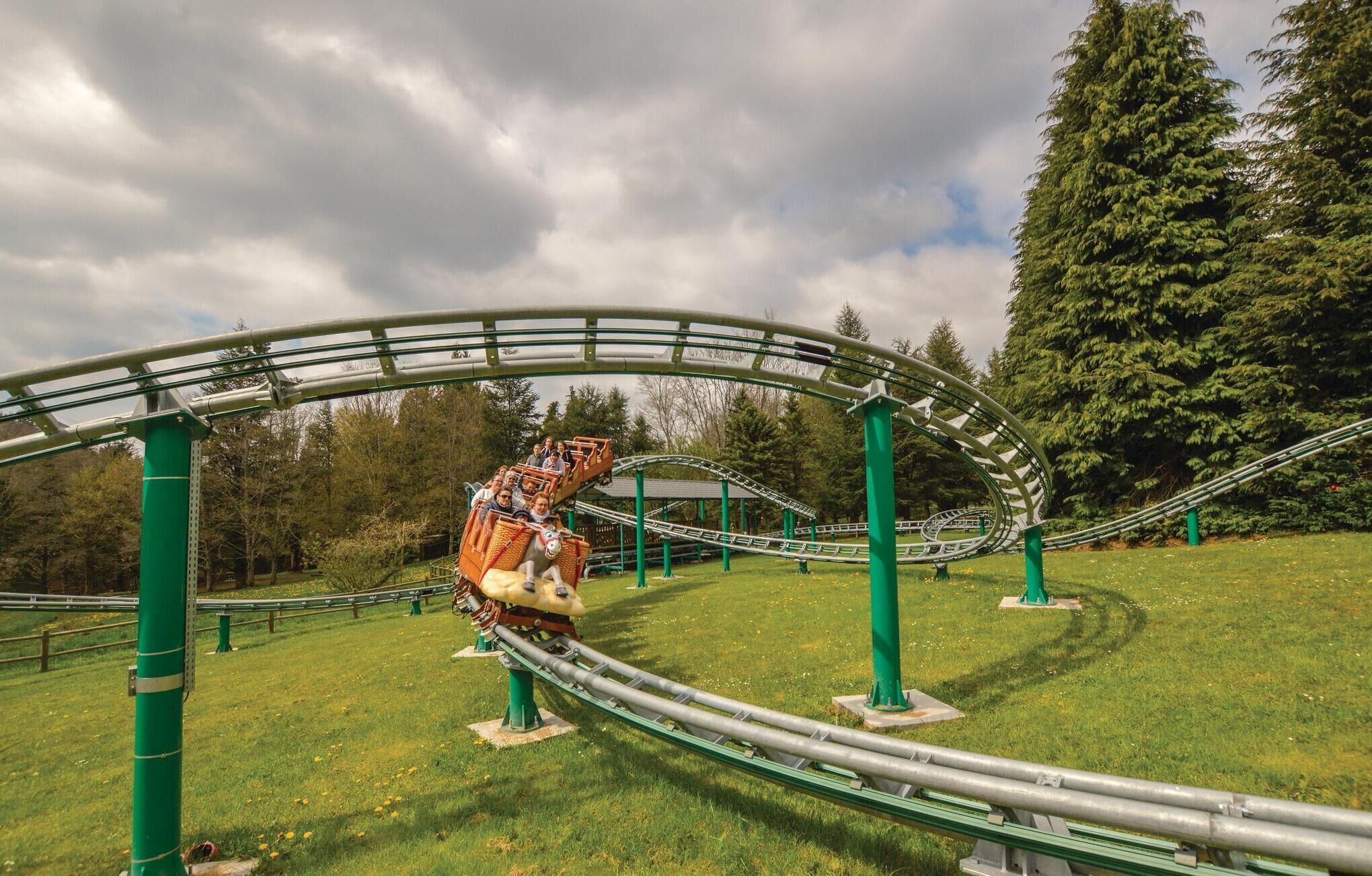 A roller coaster in a park with green supports and a grassy area.