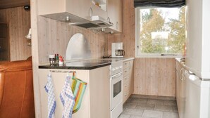 A compact kitchen with wooden walls, a stove, a coffee maker, and a window with a view of trees. - Stunning home in Middelfart with sauna (Middelfart)