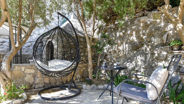A hanging chair, a metal table, and a metal chair in a stone-walled outdoor area with trees. - Awesome home in Podstrana (Podstrana)