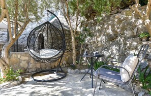 A hanging chair, a metal table, and a metal chair in a stone-walled outdoor area with trees. - Awesome home in Podstrana (Podstrana)