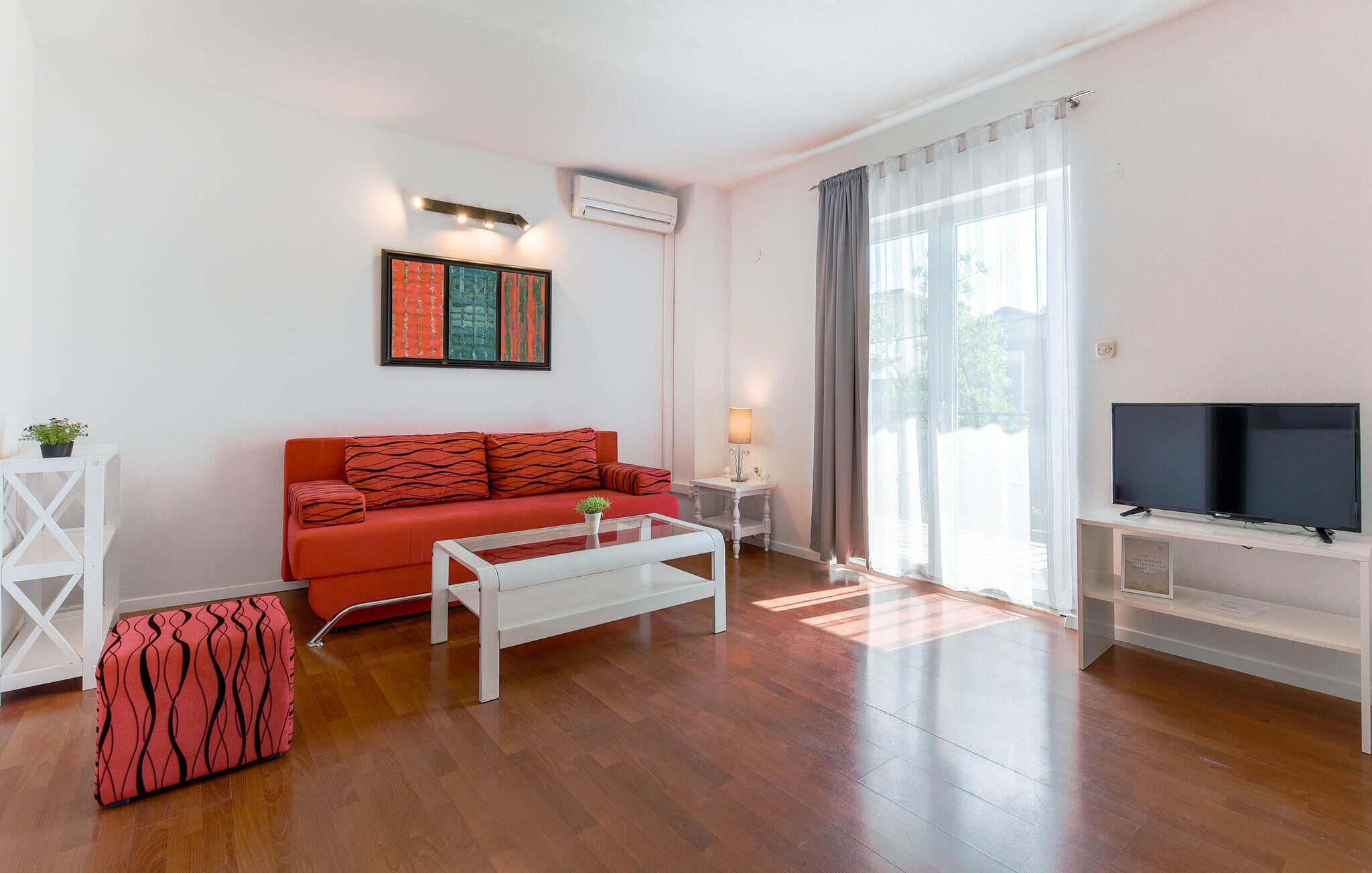 Una sala de estar moderna con un sofá rojo, una mesa de centro blanca y un televisor de pantalla plana sobre un mueble.