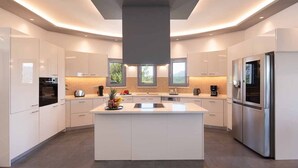A modern kitchen with a central island, stainless steel appliances, and a large window providing natural light. - Luxury villa with 2 pools , jacuzzi and tennis court (Corfu)