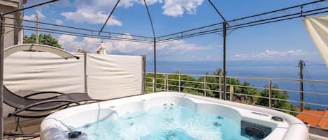 A hot tub on a balcony with a clear view of the sea and mountains.