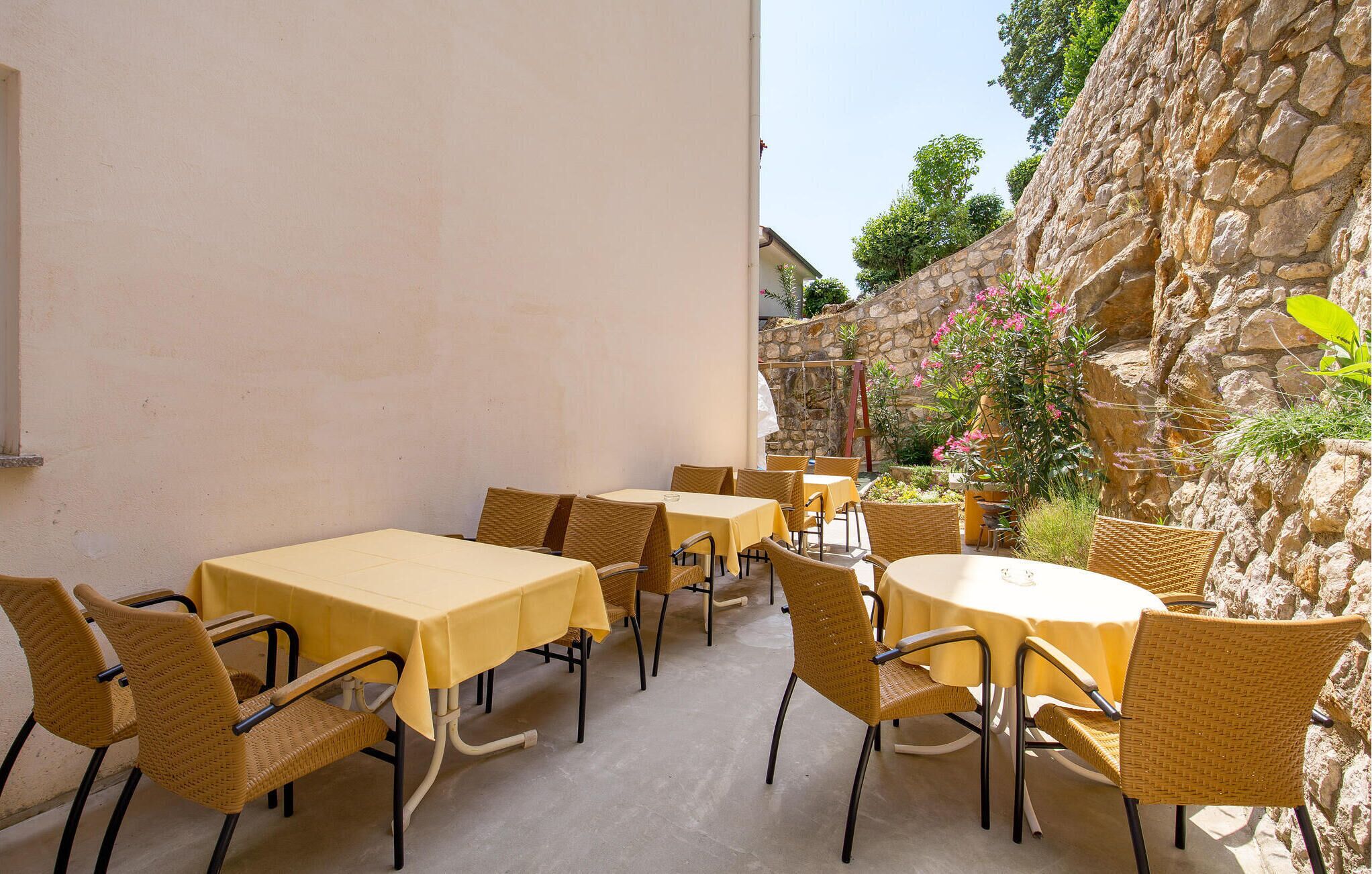 An outdoor patio with tables and chairs, surrounded by stone walls and greenery.