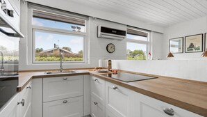 Una cucina moderna con mobili bianchi, un piano di lavoro in legno, un lavello incassato e una finestra con vista su una casa.