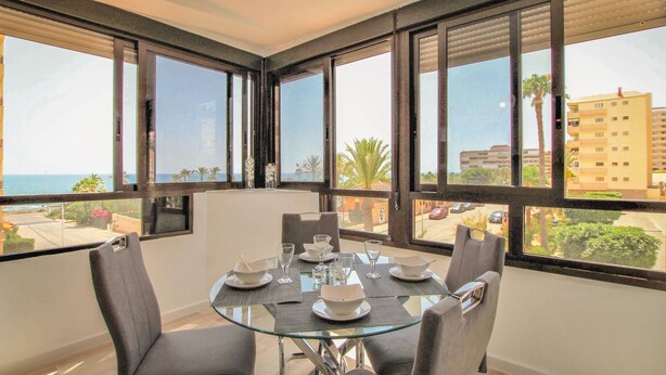 A dining area with a glass table, grey chairs, and a view of the sea and buildings. - Cozy apartment in Torrevieja with house sea view (Torrevieja)