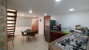 Une cuisine compacte équipée d’une cuisinière à gaz, d’un four à micro-ondes et d’un réfrigérateur. Un coin repas avec une table et des chaises est également disponible.