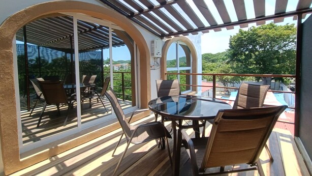 Une terrasse extérieure avec une porte vitrée donnant sur un balcon, aménagée avec une table et des chaises, et surmontée d’une pergola.