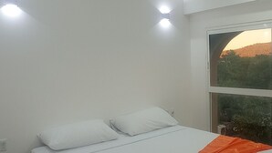 Une chambre à coucher avec un lit, des murs blancs, un ventilateur de plafond et une fenêtre donnant sur un beau paysage.