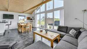 Una sala de estar moderna con un ventanal grande, una zona de comedor y un sofá gris.