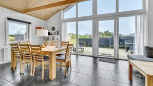 Un comedor con una mesa y sillas de madera, ventanas amplias y vistas al exterior.